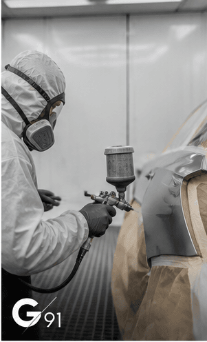 Peintre en combinaison appliquant la peinture au pistolet sur une aile en cabine de peinture